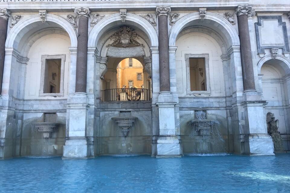 A historic building with arched windows and a fountain in front.
