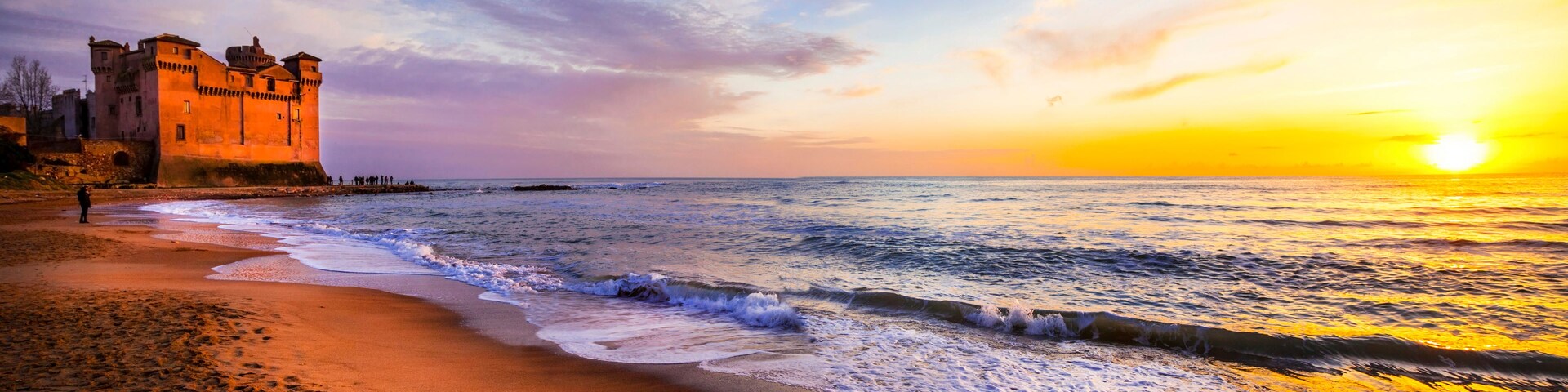 Una playa con olas, un castillo y un atardecer.