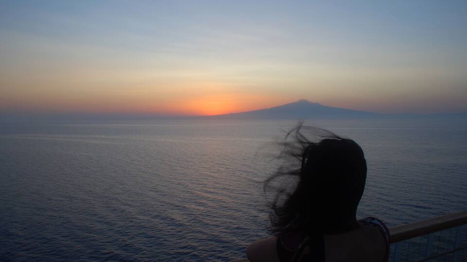 Ein Sonnenuntergang über einem ruhigen Meer mit einem Berg in der Ferne.