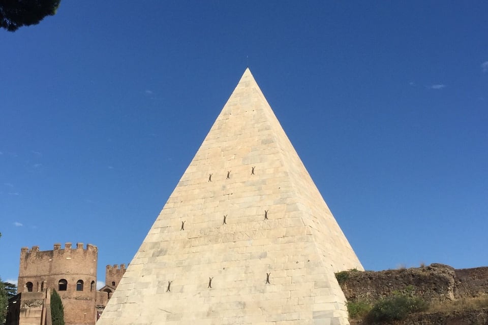 A large stone pyramid with inscriptions, surrounded by a fence and a castle in the background.