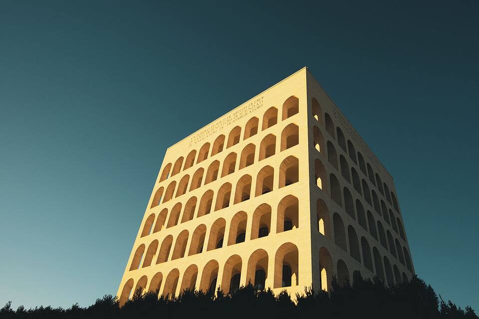 A large, square building with a grid of windows on a hill under a clear sky.