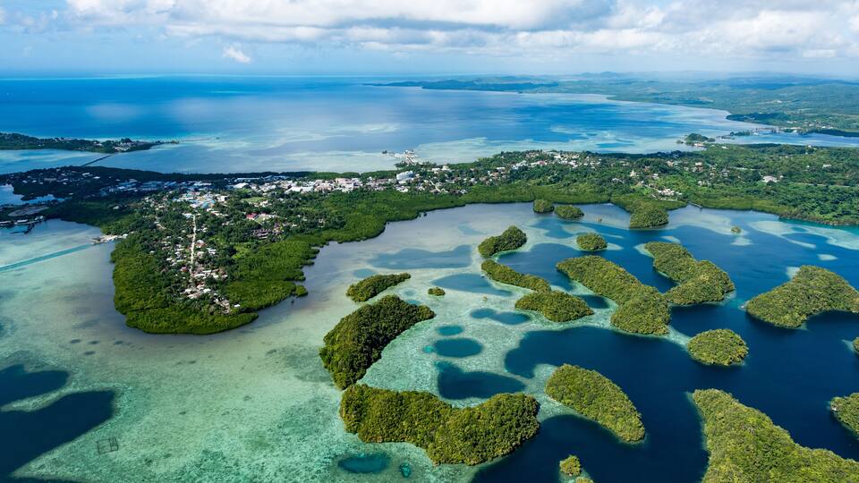 An aerial view of a coastal region with a small town, clear blue waters, and numerous green islands.