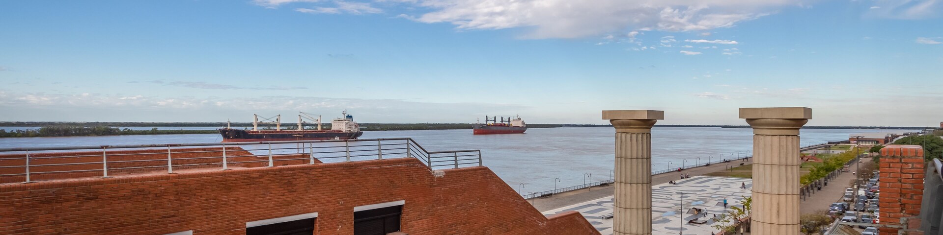 Vista para a frente marítima com um edifício de tijolos, um navio grande e céu claro.