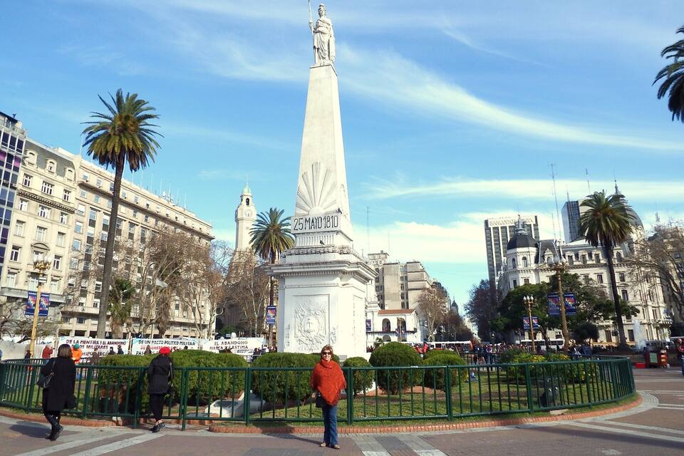 A monument with a statue, surrounded by palm trees and buildings.