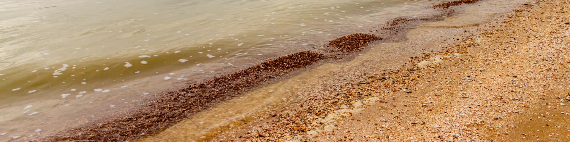 A calm sea with a pebbly beach and distant ships.