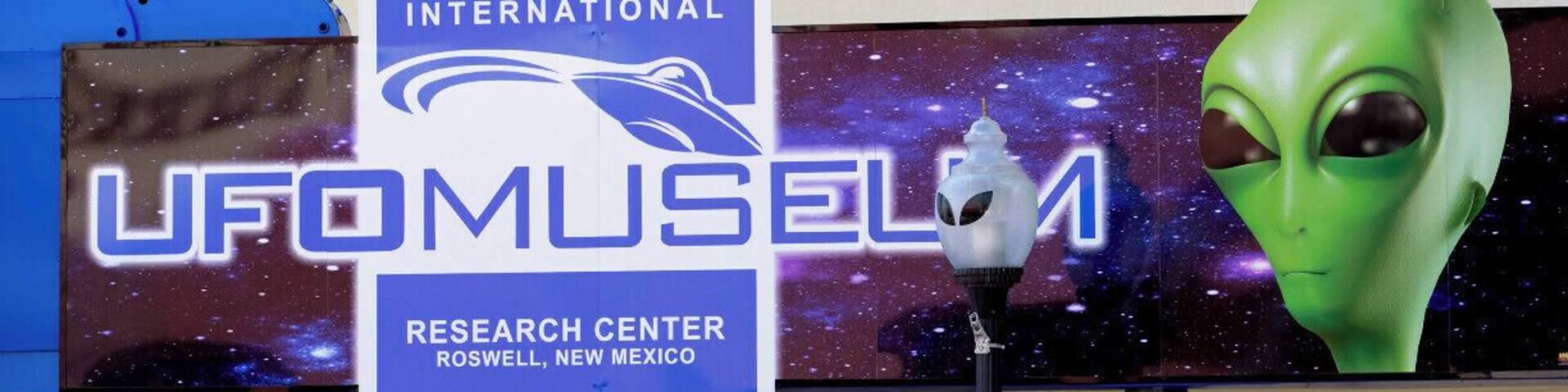 A UFO museum with a sign reading "International UFO Research Center Roswell, New Mexico" and a large alien figure.