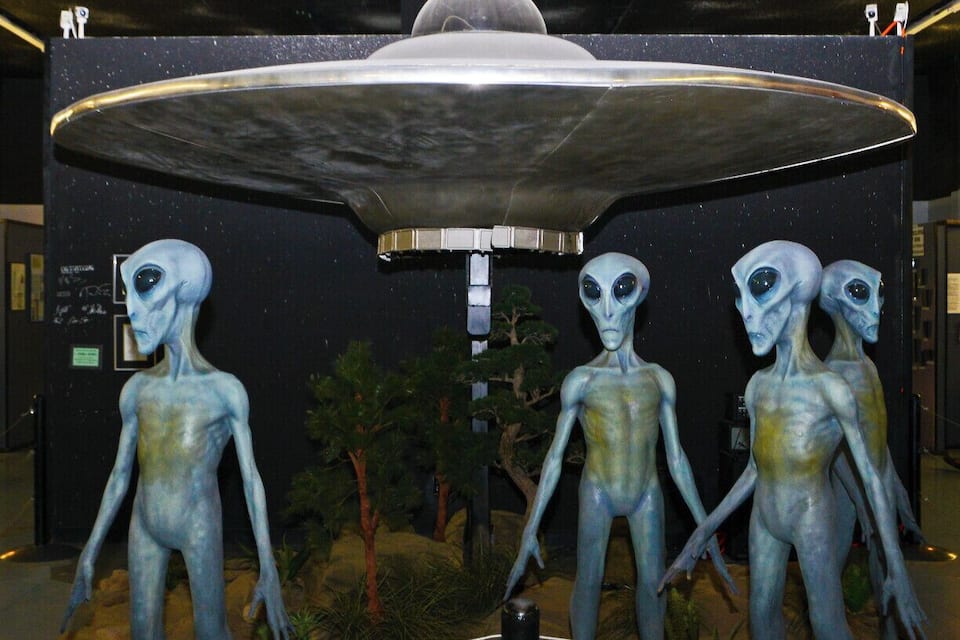 A UFO hovering above alien statues in a museum.