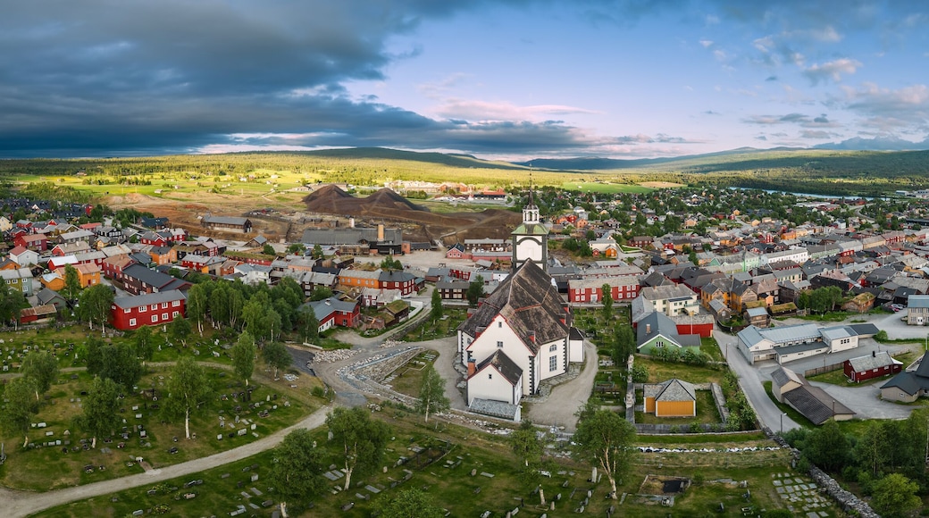 A sweeping drone panorama captures Roros, Norway, in summer splendor, with historic buildings nestled amid vibrant greenery under a dynamic sky