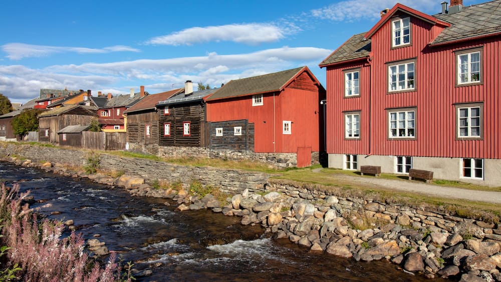 A river flowing alongside a row of traditional wooden houses with red and grey exteriors.