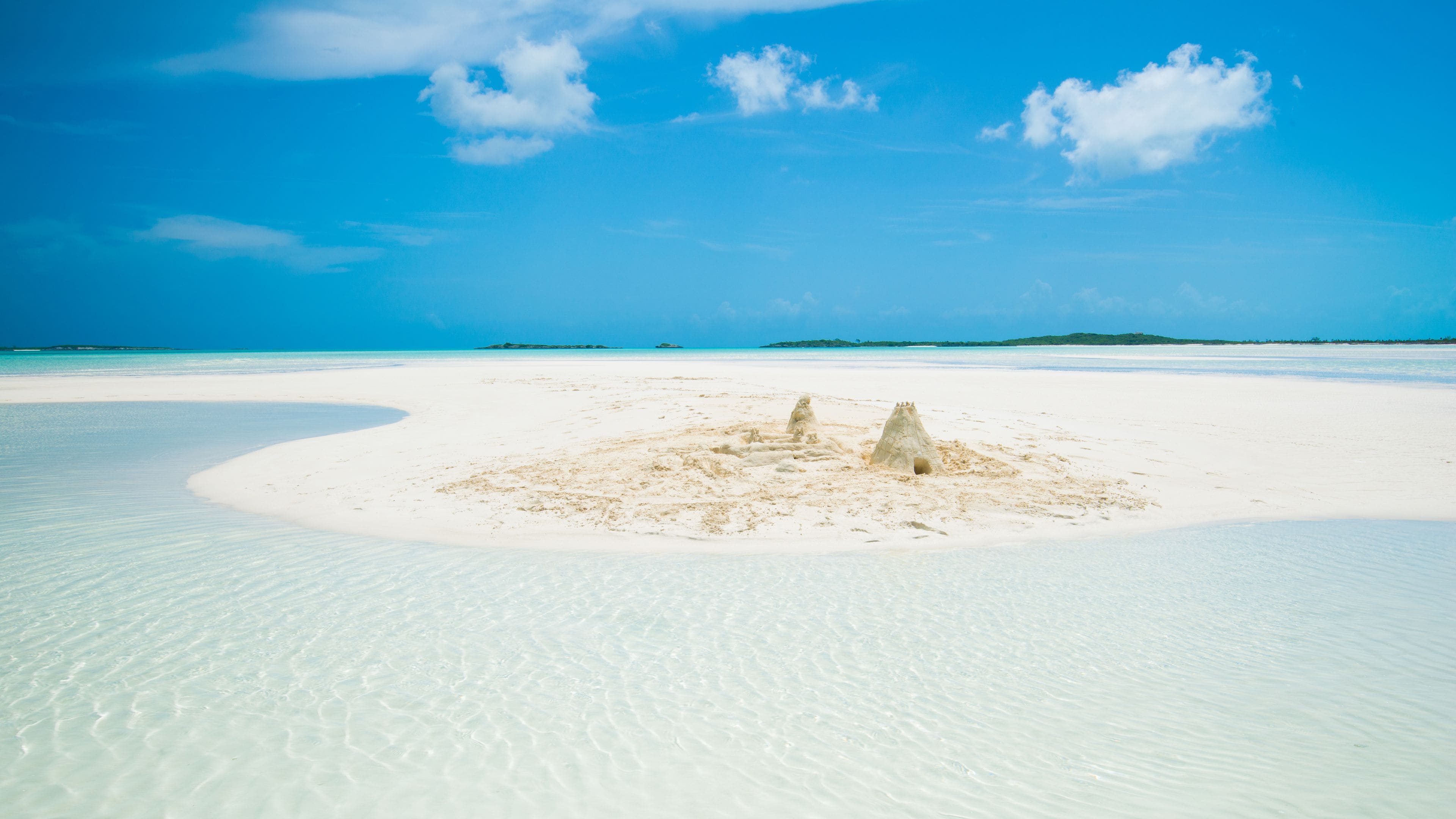 A sandy beach with clear turquoise water and a small sandcastle in the center.