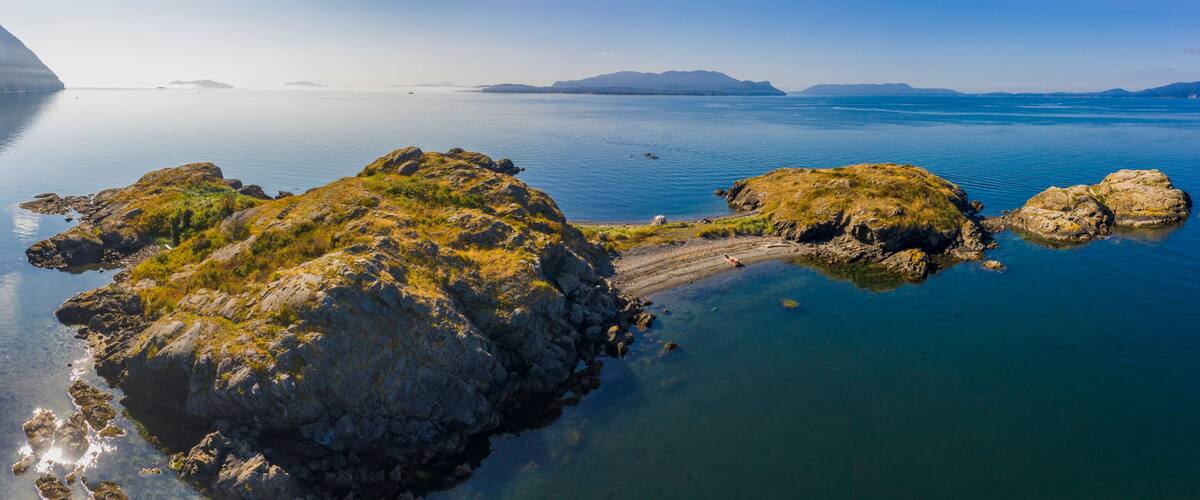 A calm lake with rocky outcrops and distant mountains.