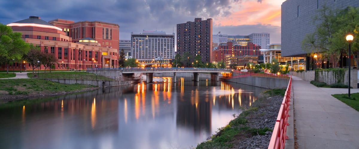 A cityscape at dusk with a river reflecting lights, modern buildings, and a bridge.