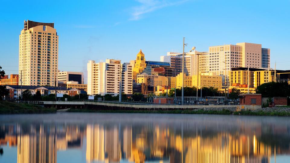 A city skyline reflected in calm water, featuring a mix of modern and historic buildings.