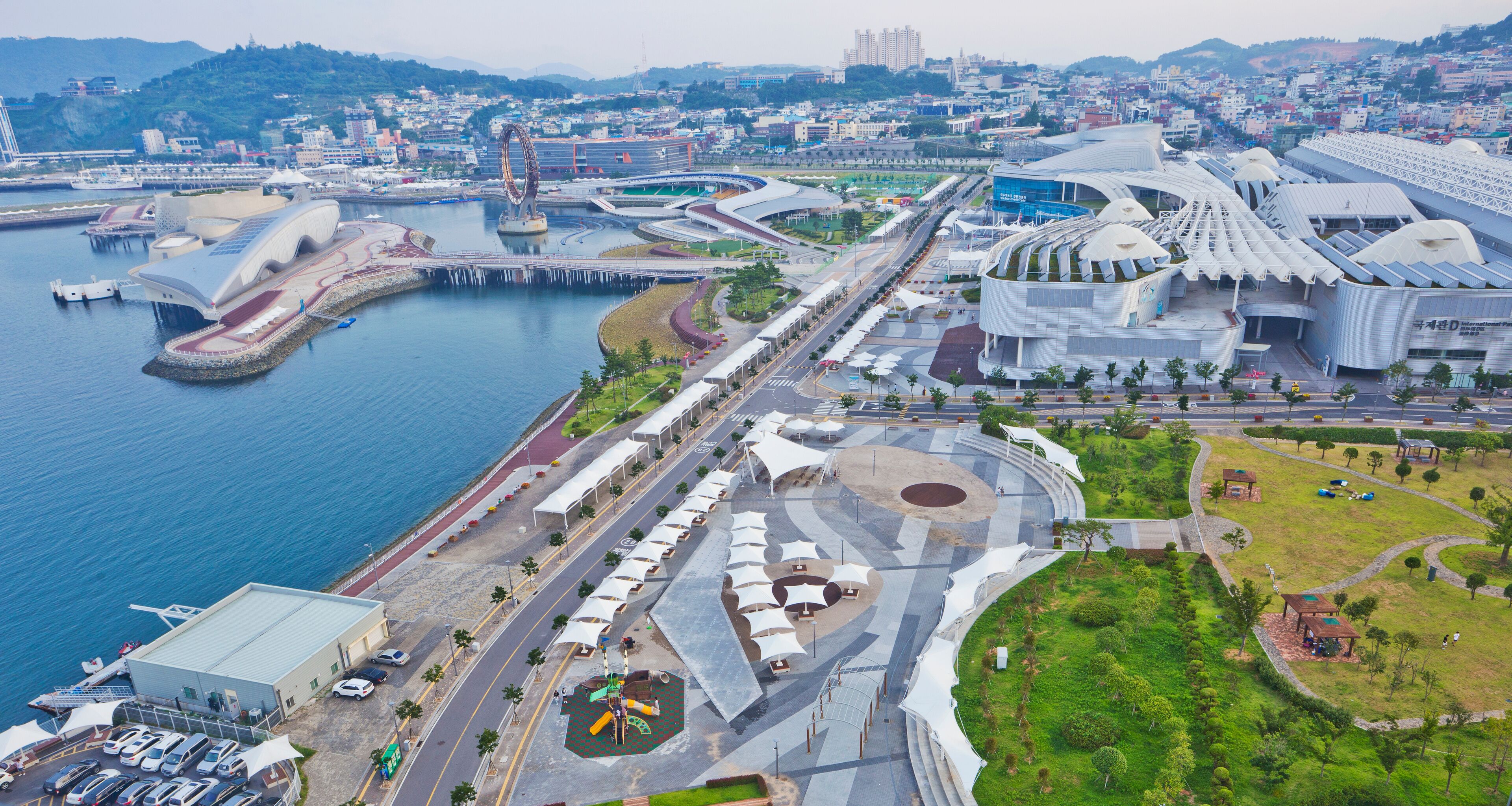 An aerial view of a modern city with a waterfront promenade, distinctive architecture, and a large stadium.
