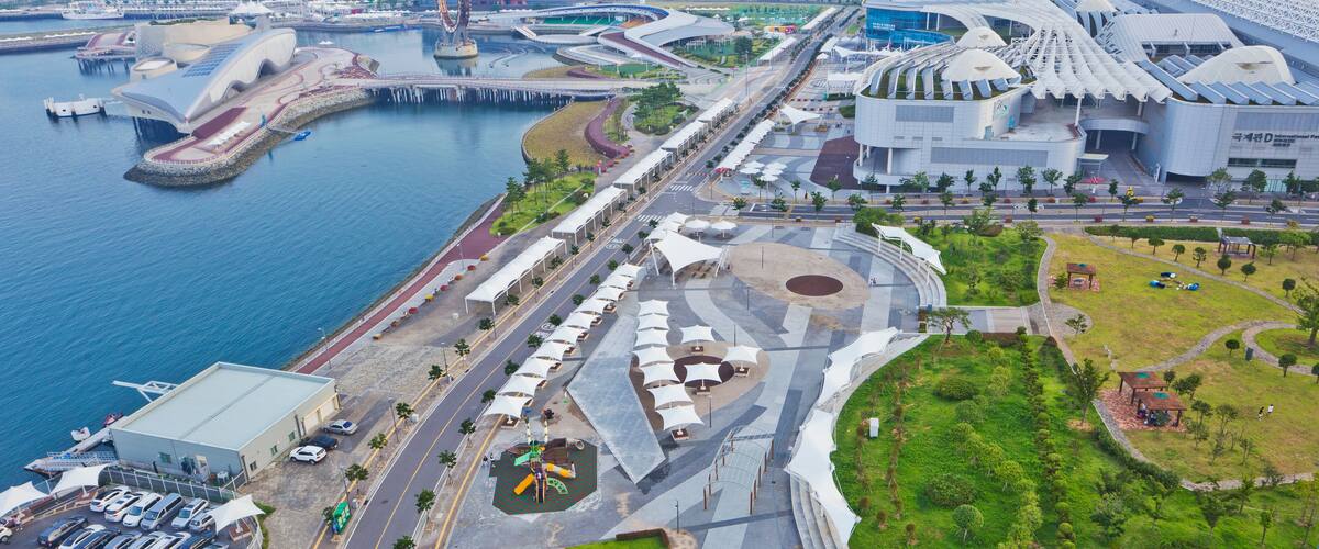An aerial view of a modern city with a waterfront promenade, distinctive architecture, and a large stadium.