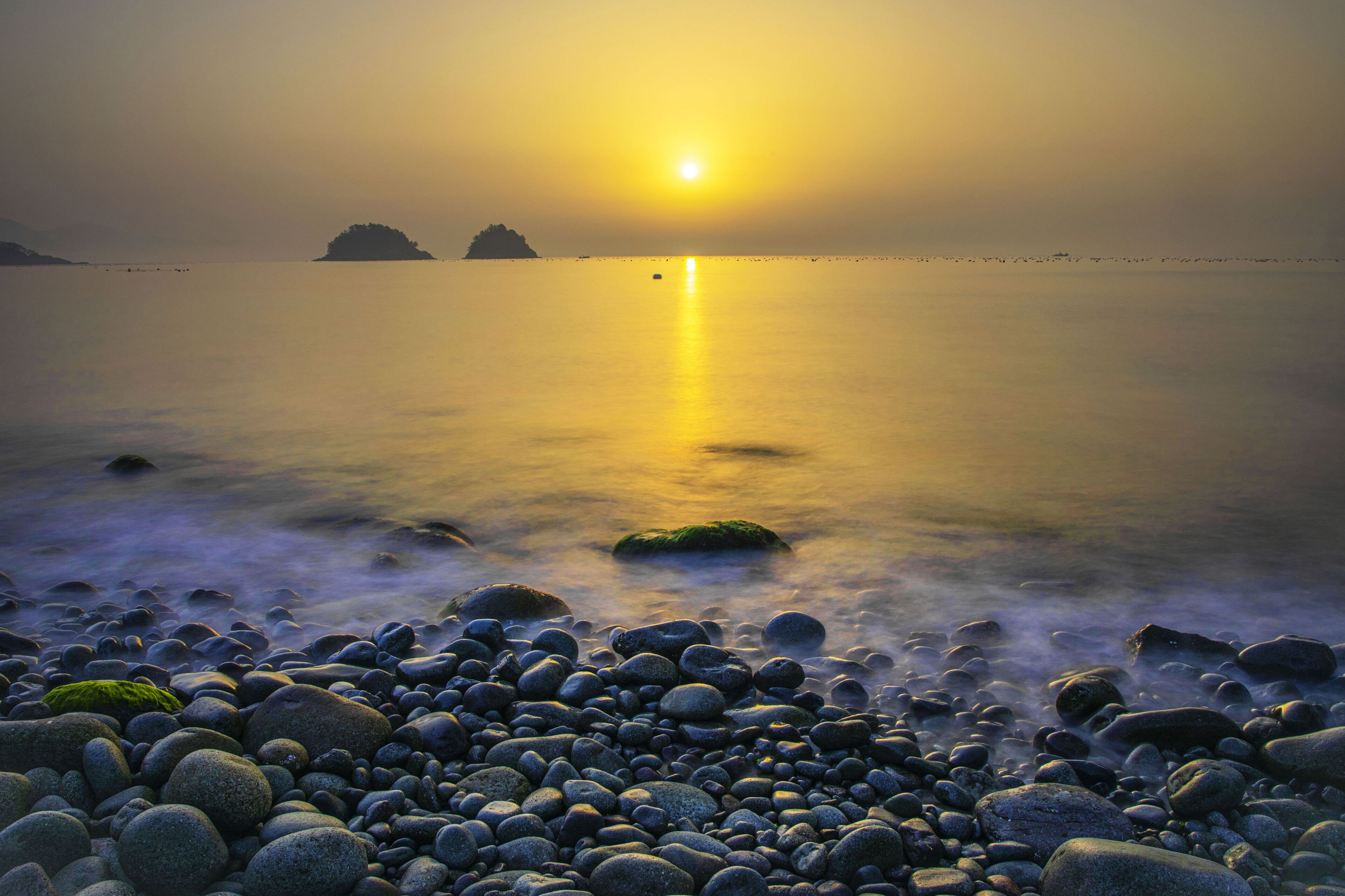 Long exposure and sunrise view of wave on pebbles against islands and horizon at Museulmog of Dolsando Island near Yeosu-si, South Korea
