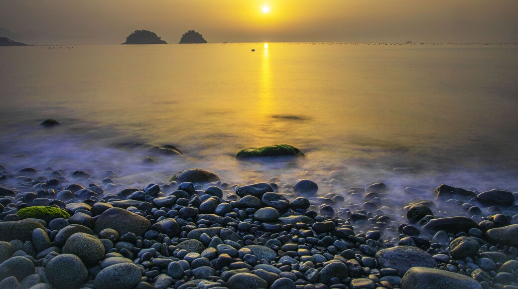 Long exposure and sunrise view of wave on pebbles against islands and horizon at Museulmog of Dolsando Island near Yeosu-si, South Korea