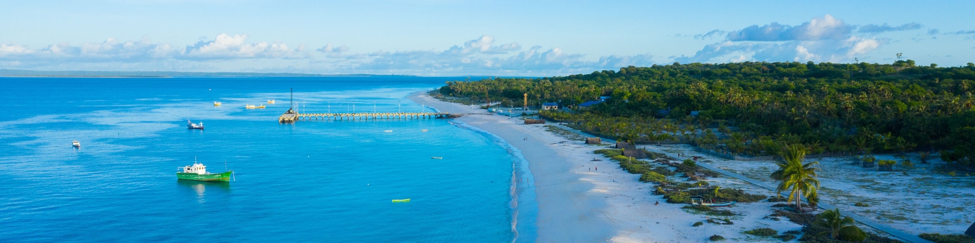 A coastal landscape with a sandy beach, clear blue waters, and a forested area.