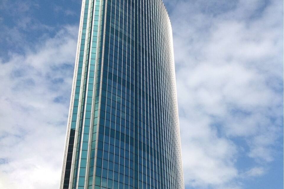 A tall, modern glass skyscraper with a curved design against a partly cloudy sky.