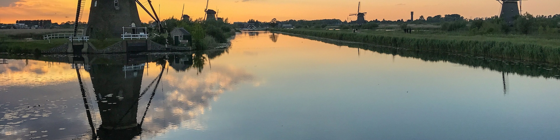 Un río tranquilo reflejando molinos de viento y un cielo al atardecer.