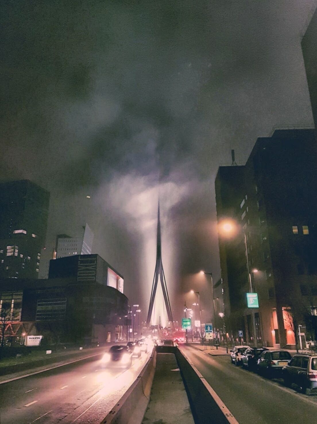 Une rue de la ville, de nuit, avec un grand pont moderne au centre.