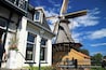 A traditional windmill with a large sail, a white building with green trim, and a yellow building with a red roof.