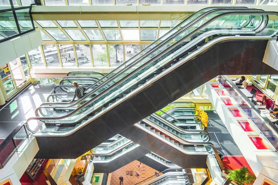 Um grande centro comercial com vários níveis, escadas rolantes e tetos de vidro.