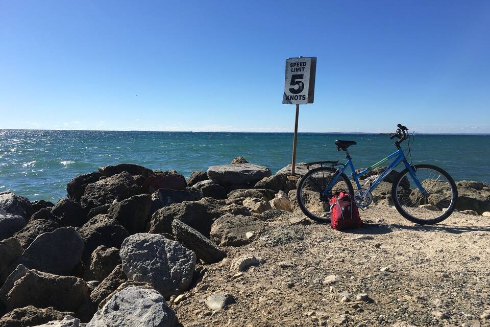 Une plage de galets avec un vélo bleu et un panneau indiquant la vitesse maximale autorisée, soit 5 nœuds.