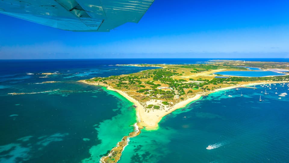 An aerial view of a coastal area with clear turquoise waters, a sandy beach, and a small island with greenery.