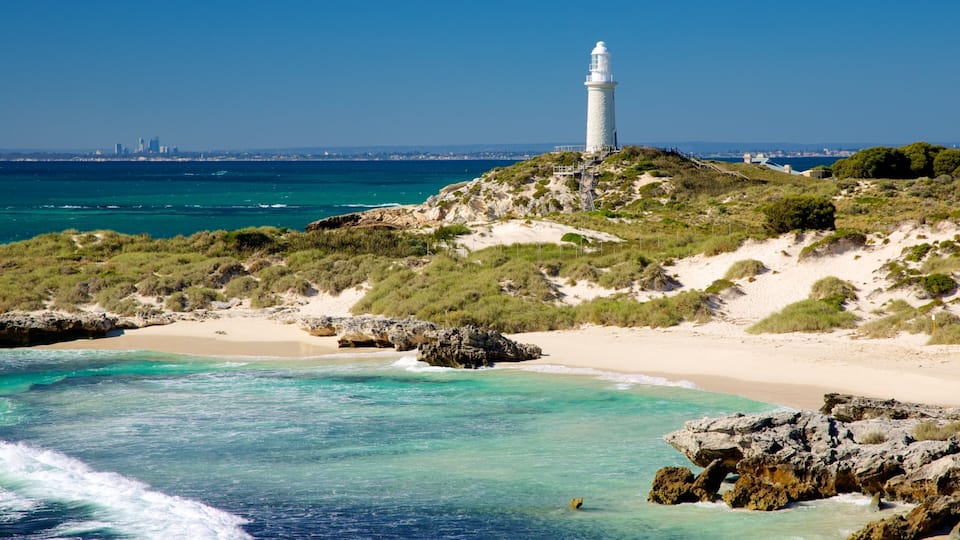 A coastal landscape with a lighthouse, sandy beach, rocky outcrops, and a clear blue sea.