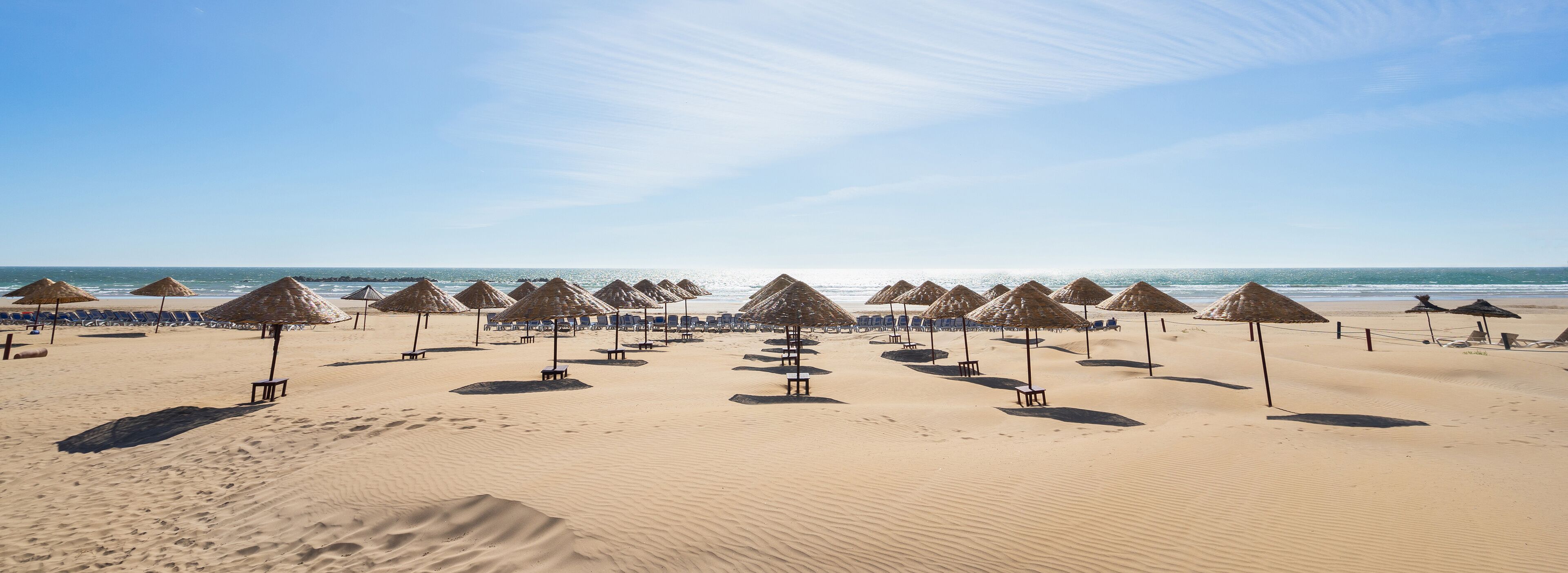 A beach with rows of thatched umbrellas and sun loungers.