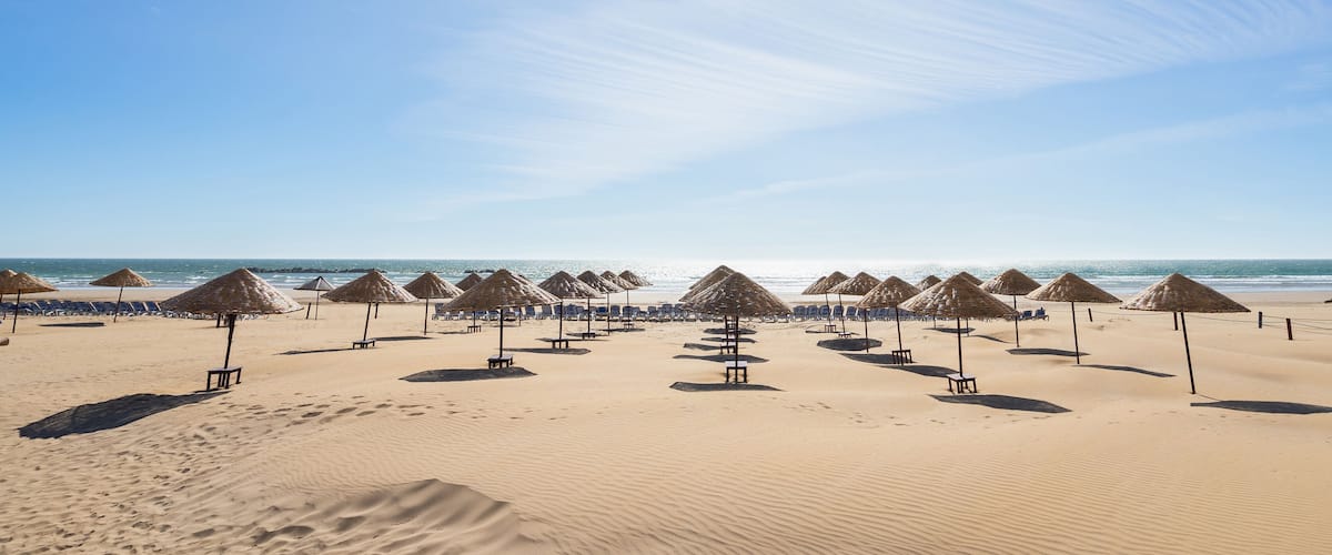 A beach with rows of thatched umbrellas and sun loungers.