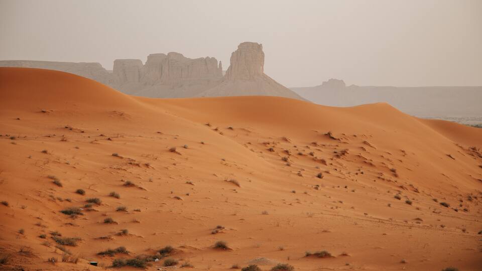 Paisaje desértico con dunas ondulantes y una formación rocosa en la distancia.
