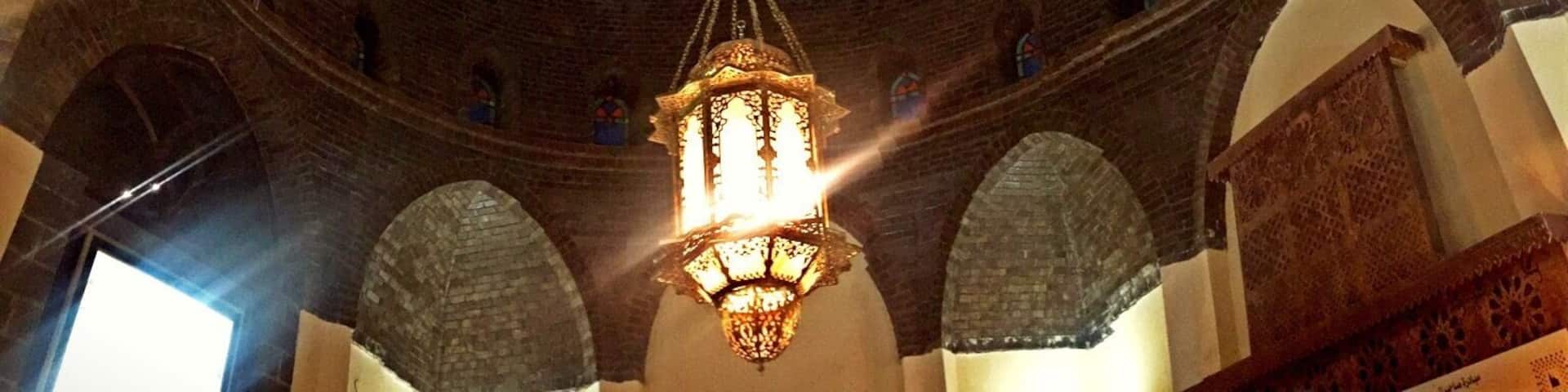 A domed ceiling with a hanging lantern, brick arches, and a patterned wall.