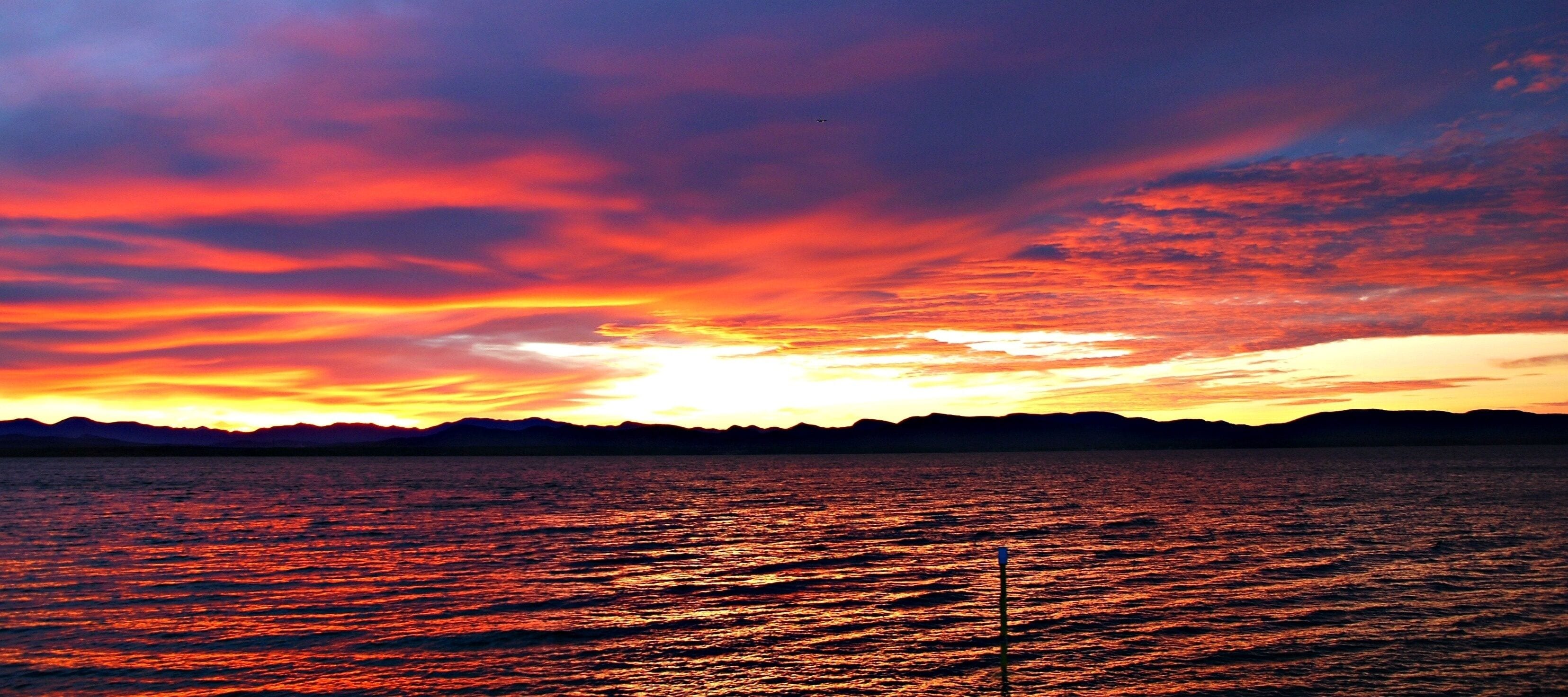 Um pôr do sol sobre a água, com a silhueta de montanhas ao fundo.