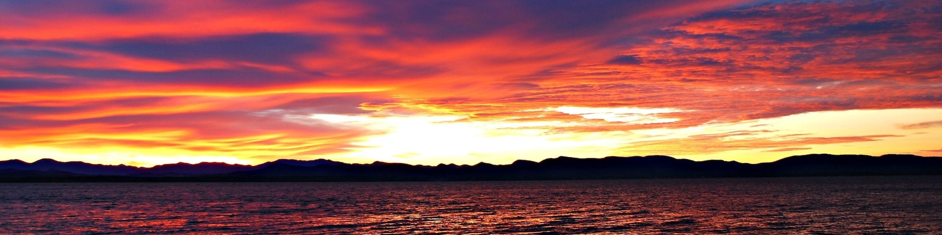 Um pôr do sol sobre a água, com a silhueta de montanhas ao fundo.
