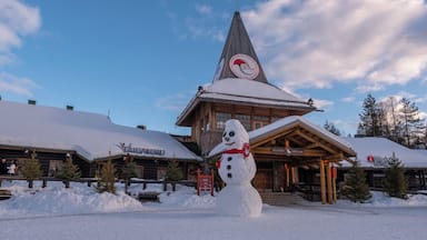 Um boneco de neve em frente a um refúgio de inverno, com uma pista de esqui ao fundo.