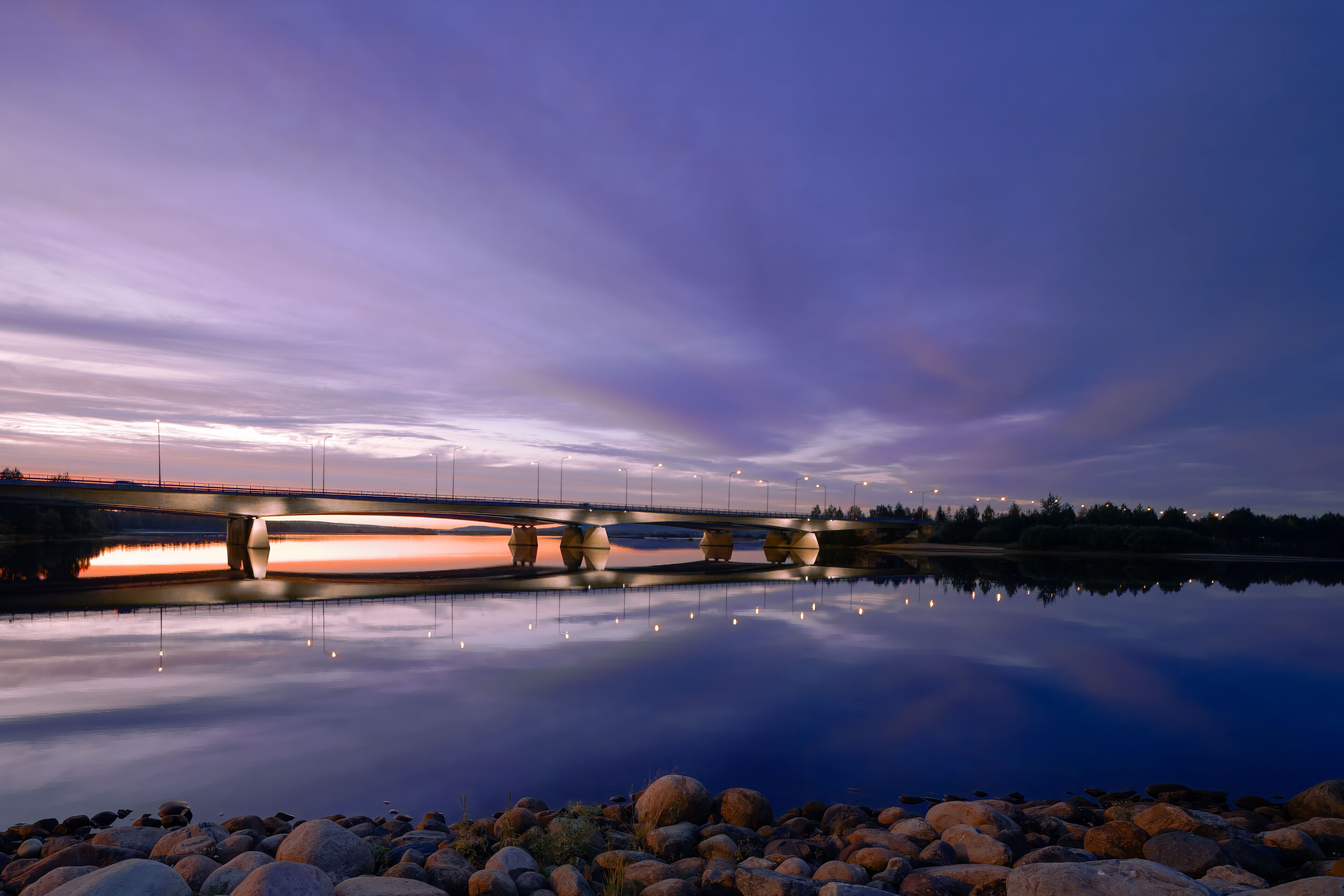 Un puente sobre una masa de agua tranquila al anochecer, con el reflejo del cielo y el puente.
