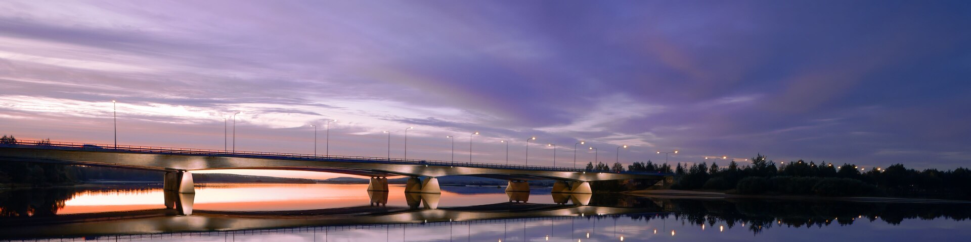 Un puente sobre una masa de agua tranquila al anochecer, con el reflejo del cielo y el puente.