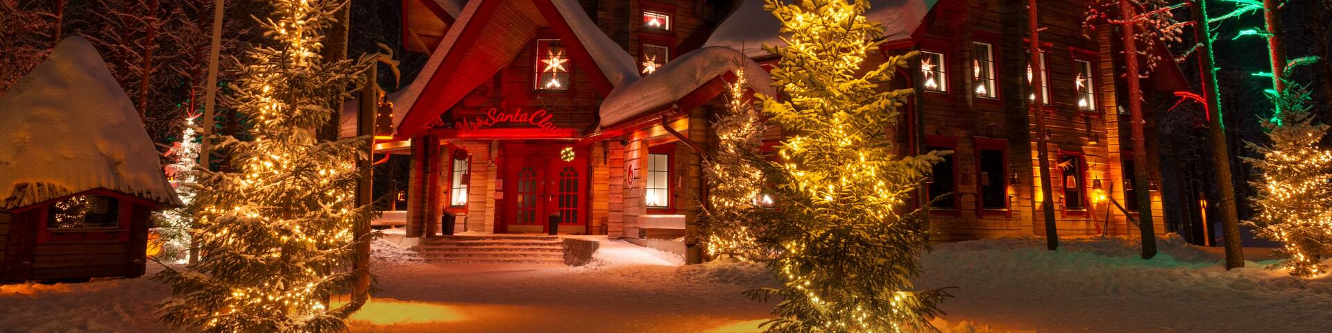 A snow-covered lodge with lit Christmas trees and a red-lit entrance.