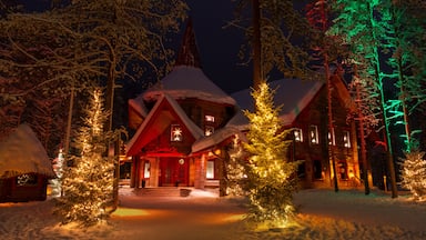 Uma cabana coberta de neve, com árvores de Natal iluminadas e entrada vermelha.