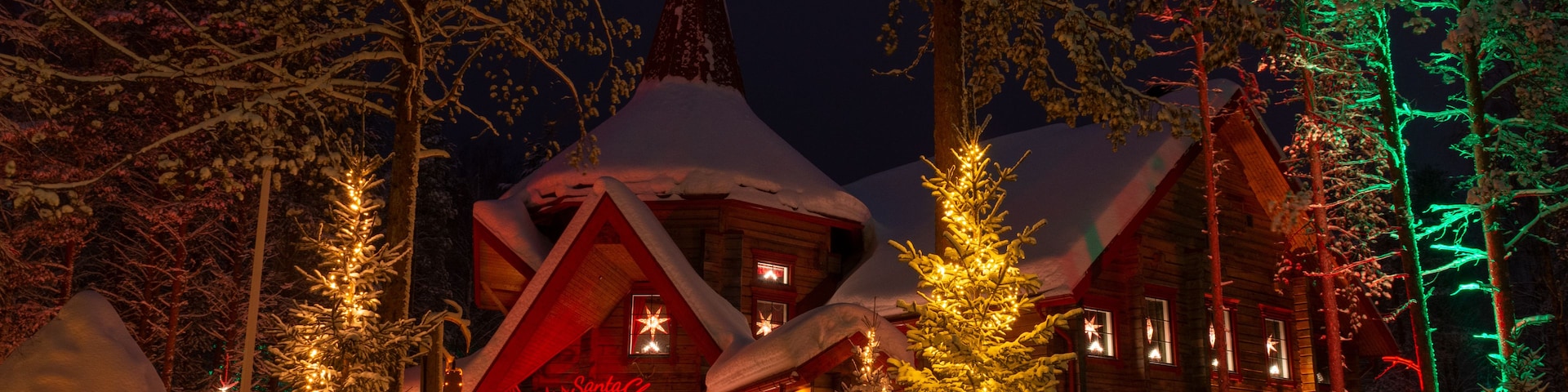 Uma cabana coberta de neve, com árvores de Natal iluminadas e entrada vermelha.