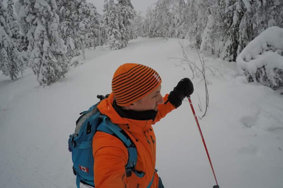 A person in winter gear with a backpack, walking on a snow-covered trail surrounded by trees.