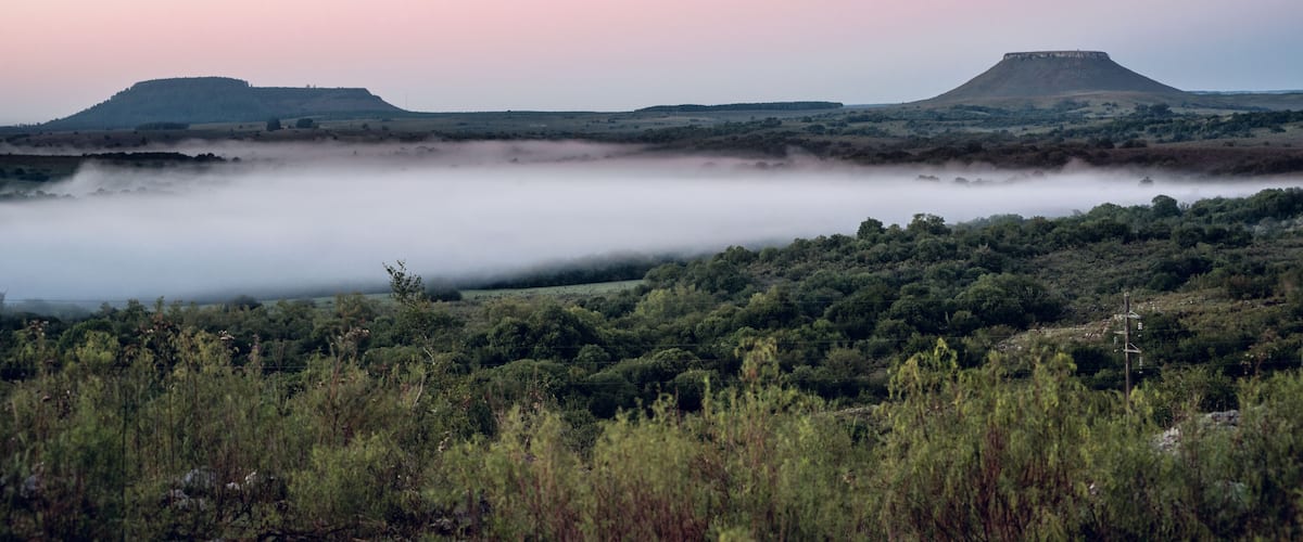 A misty landscape with rolling hills and a flat valley.