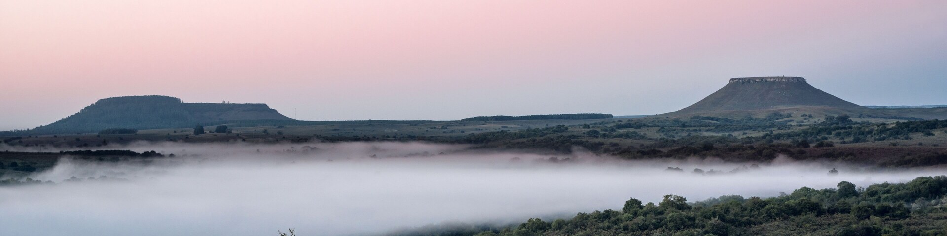 A misty landscape with rolling hills and a flat valley.