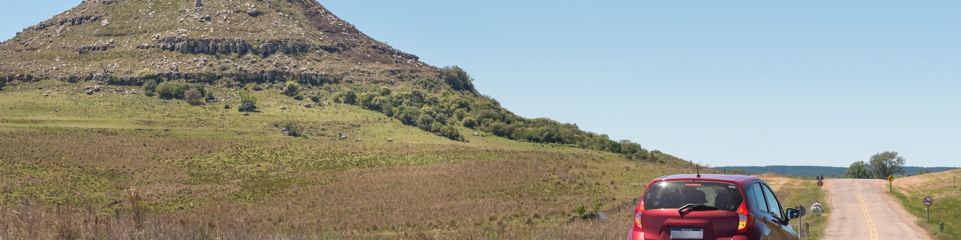 A red car is driving down a road in a grassy field