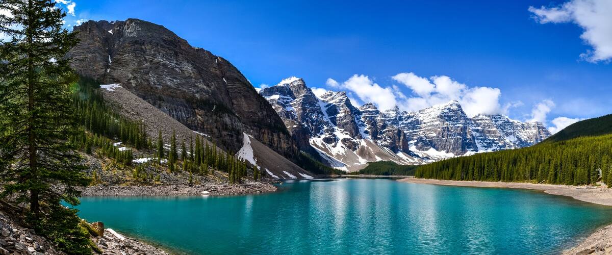 A turquoise lake surrounded by rugged mountains and dense forests.
