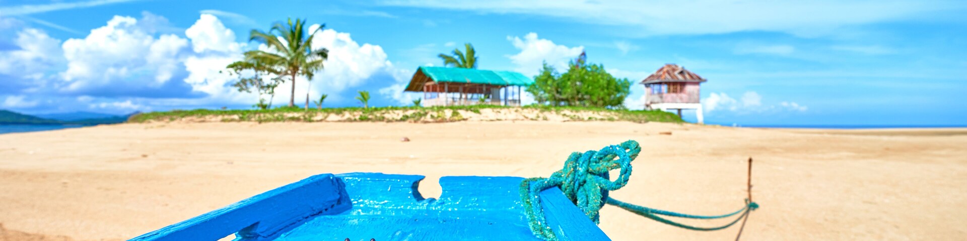 Uma praia com um barco azul, uma estrela-do-mar e casas ao fundo.