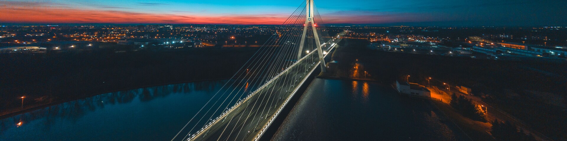 A nighttime aerial view of a cable-stayed bridge with city lights in the background.