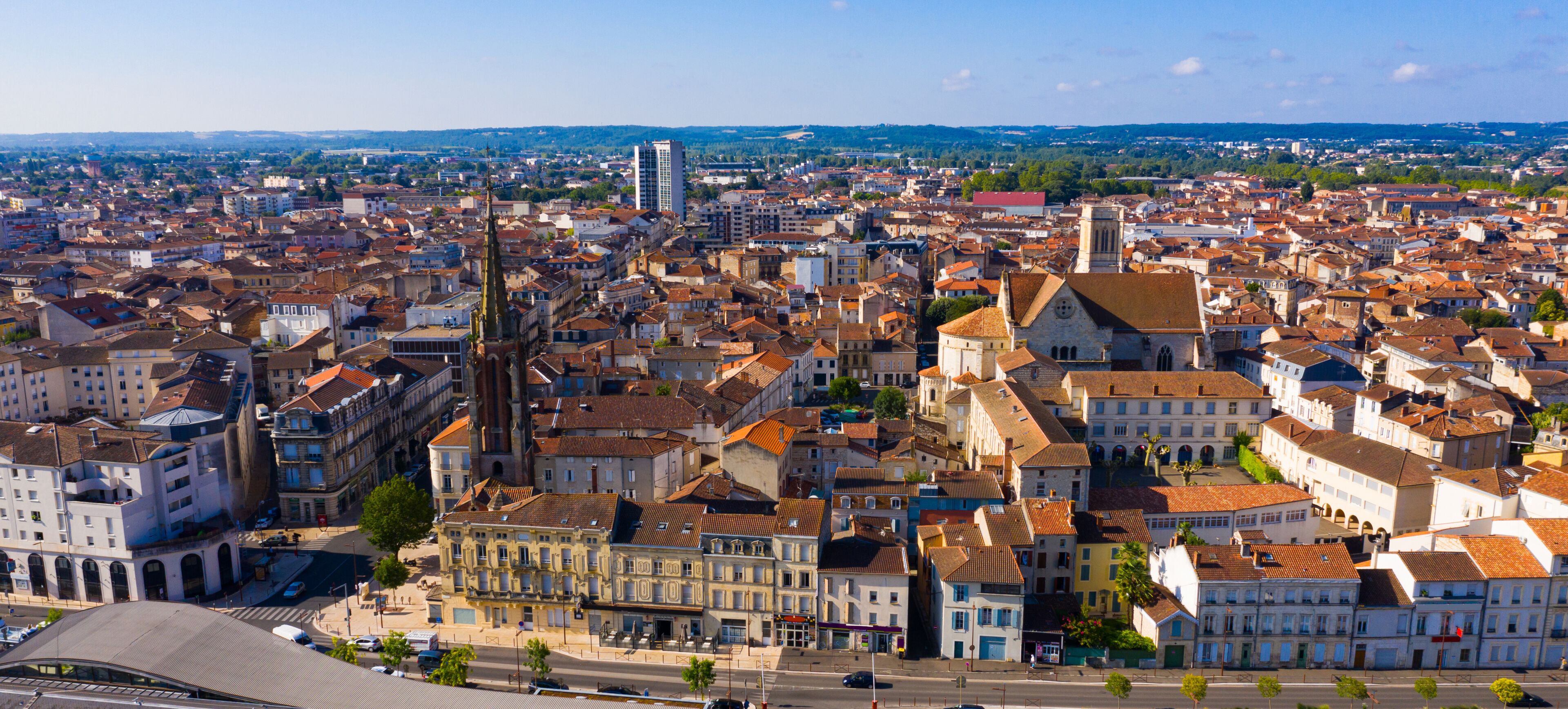 A panoramic view of a historic city with dense architecture, a prominent church tower, and a river in the distance.